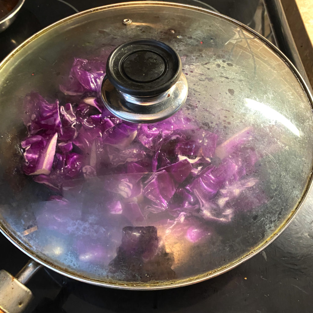 Red cabbage in a wok with a glass lid on